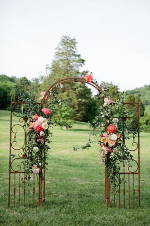 a refined vintage wedding arch made of a vintage gate, with greenery, neutral, peachy and pink blooms is chic