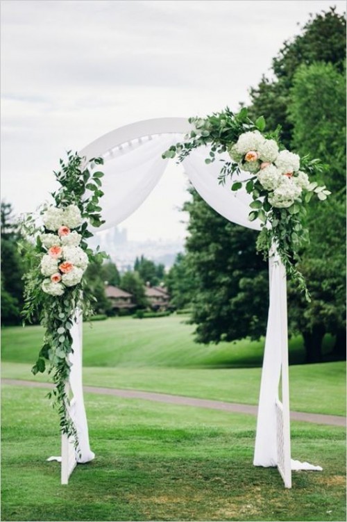 a white wedding arch with white fabric, greenery, white and blush blooms is an elegant and timeless solution