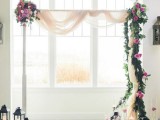 a catchy wedding arch with blush fabric, greenery, white and hot pink blooms and candle lanterns all around