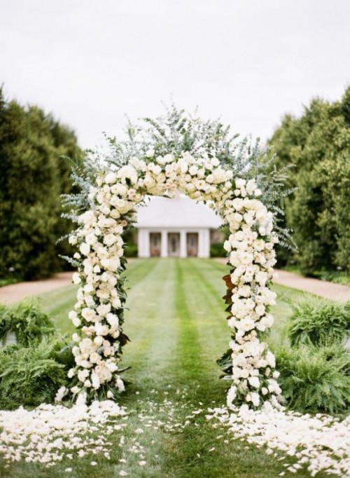 a lush and bold wedding arch covered with white blooms and eucalyptus, with petals on the ground is amazing