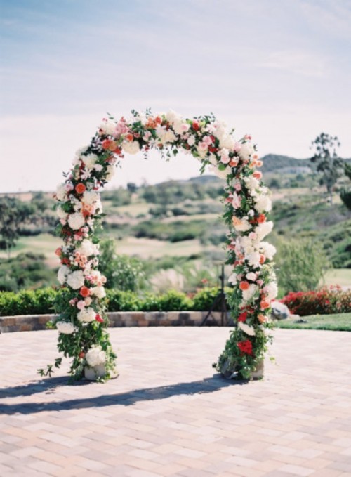 a bright and cool wedding arch with red and white blooms and greenery is a stylish and chic idea
