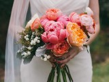 a pink wedding bouquet with peonies, blush blooms, orange flowers, greenery and berries is a stylish idea for a spring or summer wedding