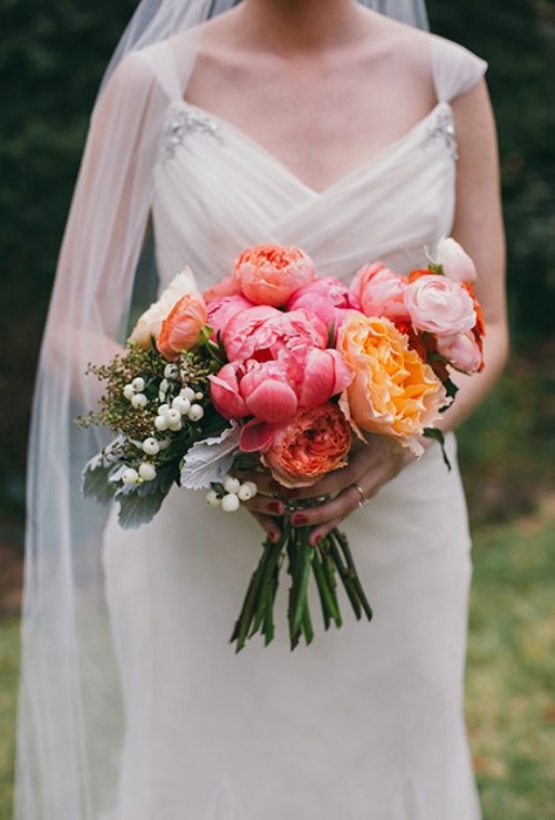 a pink wedding bouquet with peonies, blush blooms, orange flowers, greenery and berries is a stylish idea for a spring or summer wedding