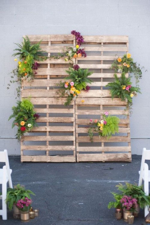 a wedding backdrop of pallets with greenery and bright blooms is a nice idea for the wedding ceremony or a photo booth