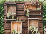 a stained pallet wood backdrop with plywood boxes with planters with greenery and succulents is a stylish idea for a rustic wedding