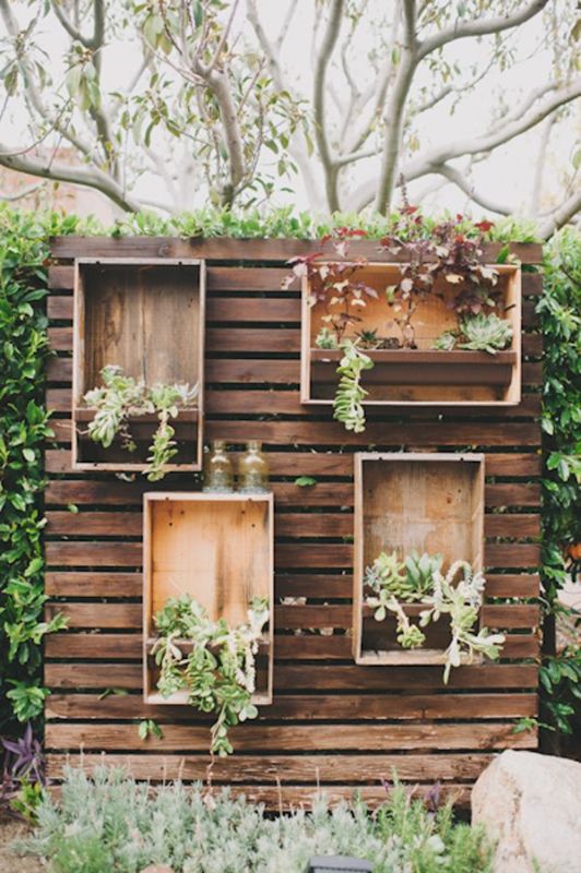 A stained pallet wood backdrop with plywood boxes with planters with greenery and succulents is a stylish idea for a rustic wedding