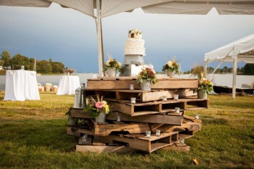 a dessert table fully made of pallets with candles, floral arrangements and a wedding cake on top