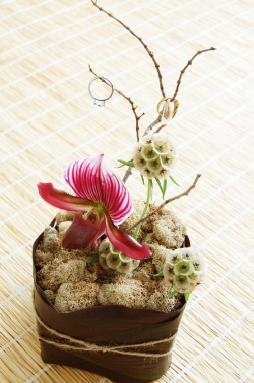 an arrangement of moss, blooms and twigs with wedding rings on top is great for an exotic wedding
