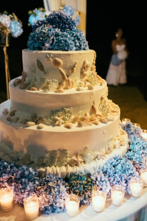 a statement beach wedding cake with sugar starfish, seashells, corals and blue hydrangeas is lovely and chic