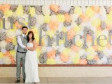 a pretty colorful yellow, peachy, grey paper pompom wedding backdrop with letters is a lovely idea that won’t break the bank