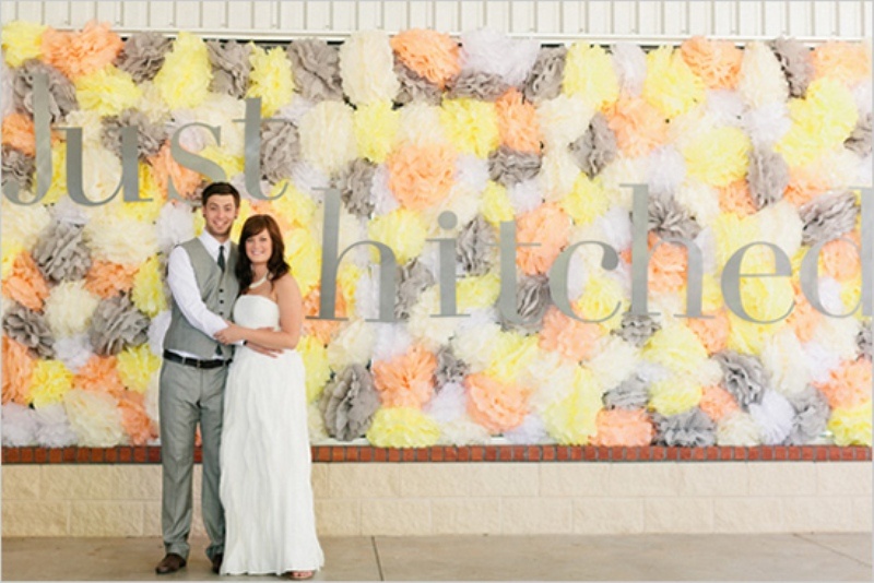 a pretty colorful yellow, peachy, grey paper pompom wedding backdrop with letters is a lovely idea that won't break the bank