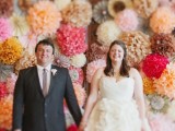a super colorful wedding backdrop composed of bright paper pompoms and balls is a lovely idea for a modern party-inspired wedding