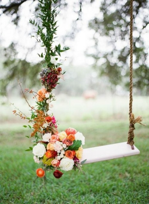 a swing decorated with greenery and bold blooms for a garden wedding is a cool place to take pics