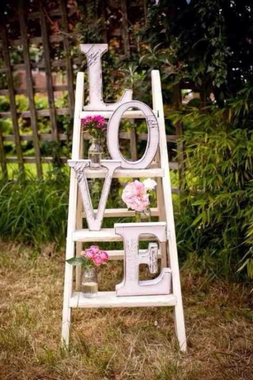 a white ladder with pink and neutral blooms and letters is a cute garden wedding decoration to rock