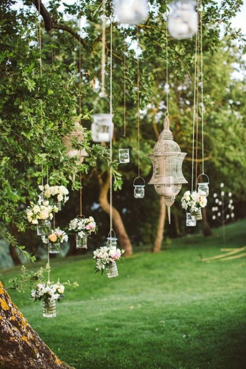 a tree with hanging jars with blooms and greenery, lanterns and candle lanterns is a pretty idea for a garden wedding