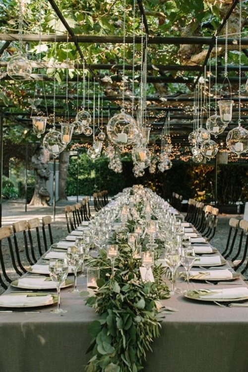 a chic garden wedding with lots of greenery, a neutral wedding tablescape with a greenery runner and candles and candle bubbles hanging over the tables