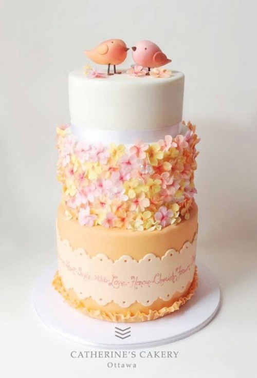 a bright wedding cake with several tiers, with sugar blooms attached to one tier and funny and cute love bird cake toppers