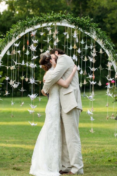 an arch covered with greenery and with paper crane garlands hanging down symbolizes happiness and love