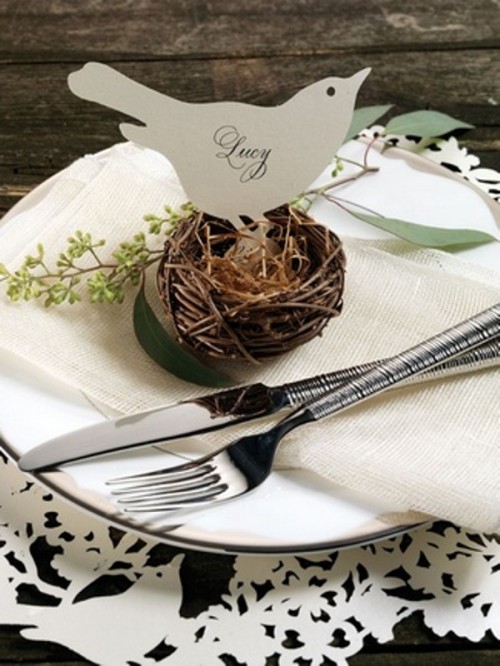 a spring wedding place setting with a neutral plate and napkin, with a nest with a paper love bird and some greenery for a neutral wedding