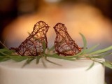 a white wedding cake topped with greenery and small vine love birds is a cool and chic idea for a wedding, it looks super cute