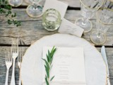 have amazing non-covered weathered wood tables decorated with greenery and accented with gilded edge glasses, plates and gold cutlery