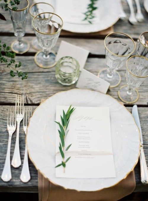 have amazing non-covered weathered wood tables decorated with greenery and accented with gilded edge glasses, plates and gold cutlery