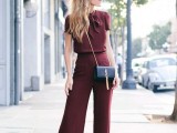 a burgundy jumpsuit with a fitting bodice and palazzo pants, a black mini bag and black heels for a fall or winter wedding