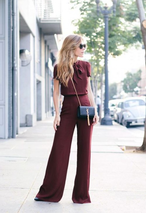 a burgundy jumpsuit with a fitting bodice and palazzo pants, a black mini bag and black heels for a fall or winter wedding