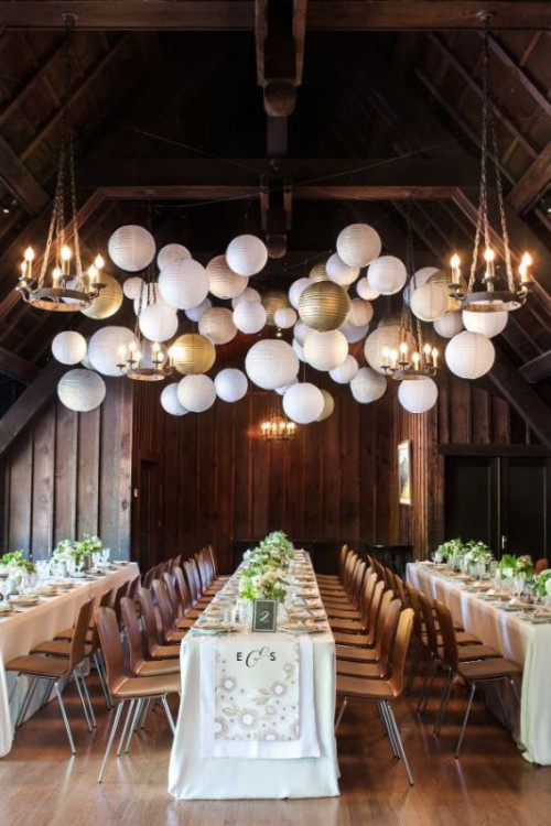 a whole arrangement of pendant paper lamps of white and gold plus chandeliers is a lovely idea to illuminate a wedding reception space
