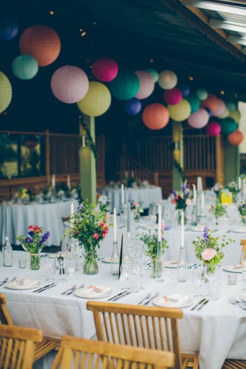 a stylish and bright summer wedding reception space with colorful floral arrangements on the tables and bright paper lamps that match in color is lovely