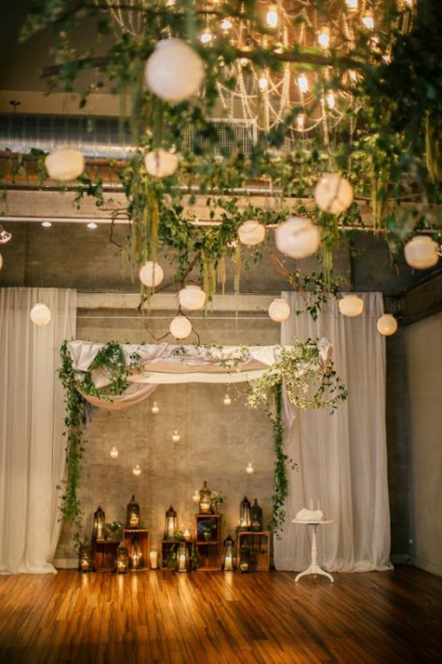 neutral paper pendant lamps and greenery plus string lights look nice in this wedding space and add light and create a mood in the space