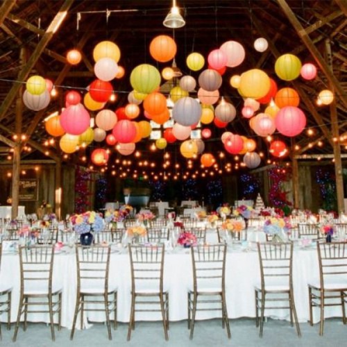 a bright wedding reception with a colorful paper lamp arrangement and string lights over the space is a lovely idea for a relaxed and laid-back wedding