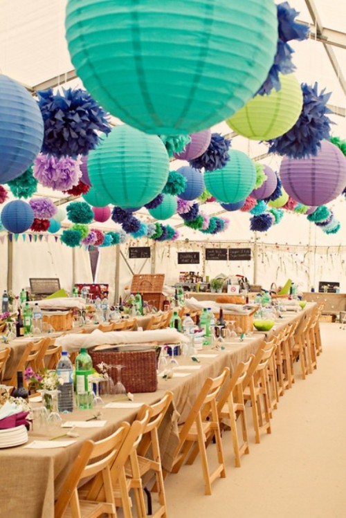 a boho rustic wedding reception with colorful paper lamps over it and pompoms to add lights, texture and color to the space