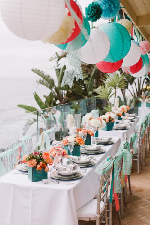 a bright tropical wedding reception space with bold blooms in teal planters, with white, teal and coral paper lamps over the space is a lovely idea