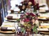 an elegant wedding tablescape with gold chargers, purple and blush blooms and greenery, plum-colored napkins and a table runner
