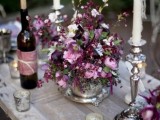 a lovely relaxed wedding tablescape with a plum and lilac-colored floral centerpiece and candles is a chic idea for a fall wedding