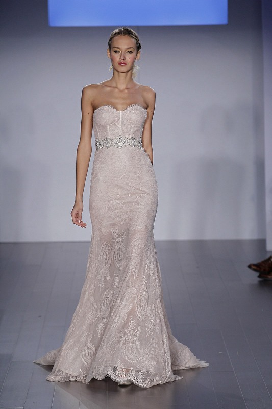 A blush strapless wedding dress with a corset bodice, a semi sheer skirt with a train and an embellished sash