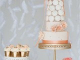 a glam dessert table with a pastel wedding cake and a macaron tower on top, with some cupcakes, and fresh peachy blooms is ideal for a glam wedding