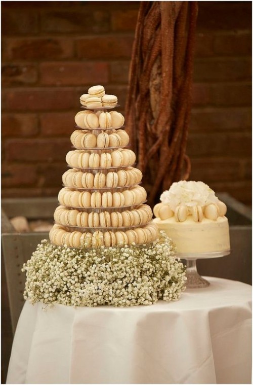 a neutral and glam wedding dessert table with a neutral wedding cake, macarons and blooms on top and an additional neutral macaron tower with baby's breath is amazing