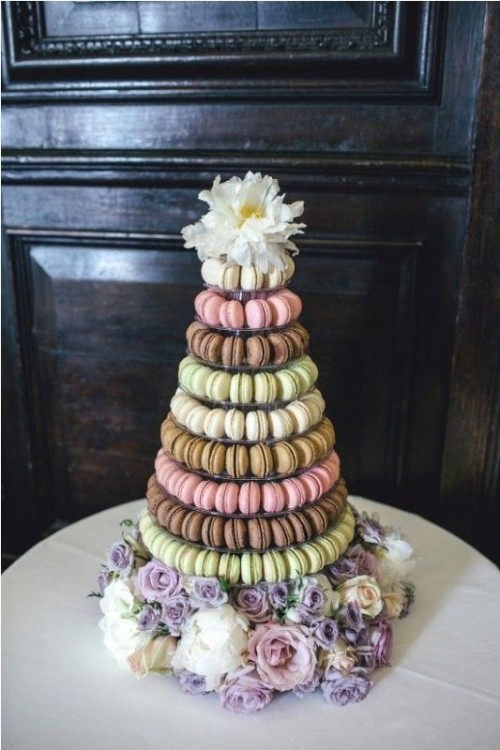 a large macaron tower that includes light pink, green and brown macarons and pastel and white blooms for decor is a gorgeous idea