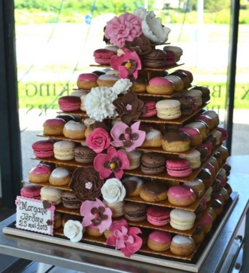 an extra large macaron tower built on a wooden stand, with lots of colorful macarons and glazed donuts plus sugar blooms is an alternative to a wedding cake