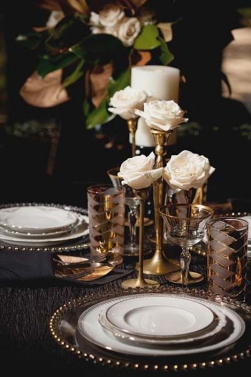 a beautiful glam and refined art deco wedding tablescape with a navy tablecloth, gold rim plates, gold cutlery and gold vases with white roses