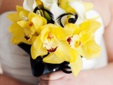 a bold wedding bouquet of yellow orchids, white callas, billy balls and black feathers plus a black wrap is a chic and whimsy idea
