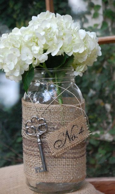 a rustic wedding centerpiece of a jar wrapped with burlap, a vintage key for an accent and white hydrangeas is great for a rustic wedding