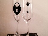 a pair of simple flutes decorated with a lock and a key is a cool and fun idea for a wedding, accent the couple’s glasses this way easily yourself