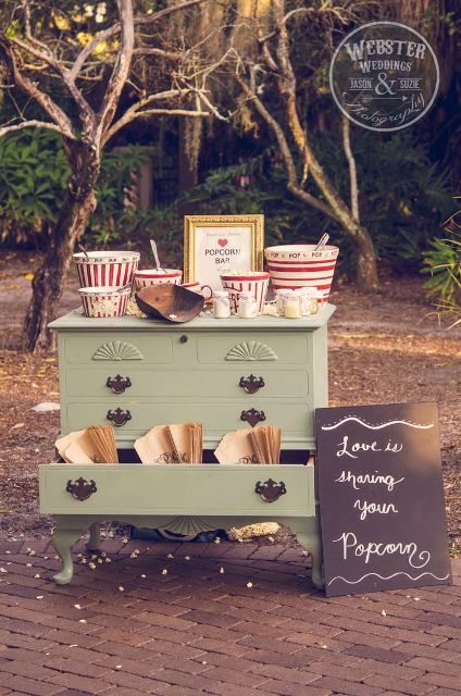 a fun retro-inspired popcorn bar with a vintage dresser, colorful striped popcorn buckets, paper bags and a chalkboard sign