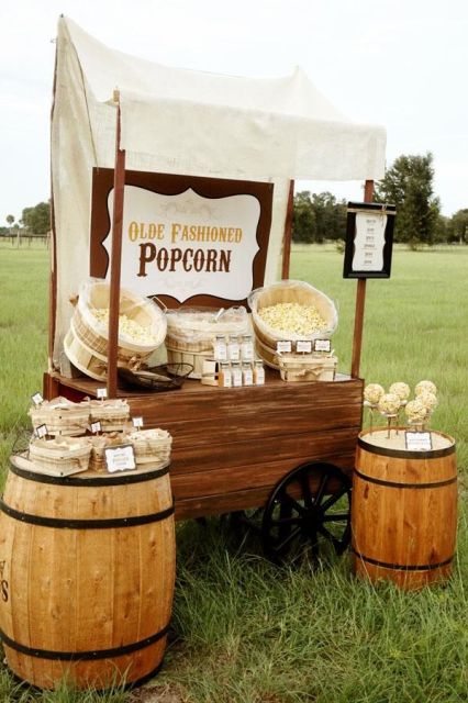 a rustic meets vintage popcorn bar with a wagon with popcorn in wooden baskets and barrels with more sweets around