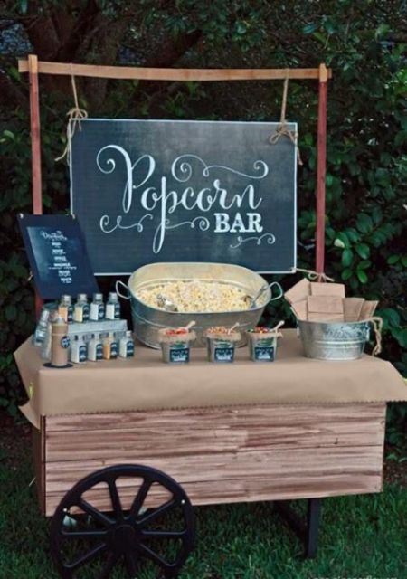 a vintage rustic popcorn bar with a trolley covered with kraft paper, popcorn in a bucket, paper bags and a large chalkboard sign
