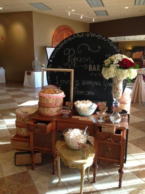 a vintage-inspired popcorn bar with a dresser, a coffee table, vintage suitcases, a chalkboard sign and boxes and bowls with popcorn