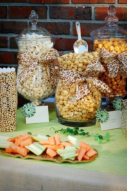 a simple and bright popcorn bar with various types of popcorn in glass jars with lids, leopard print bows and leopard print paper bags